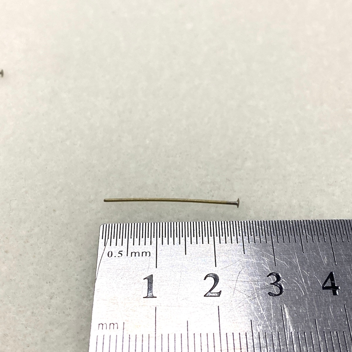 Small metal head pin next to a ruler on a textured white background
