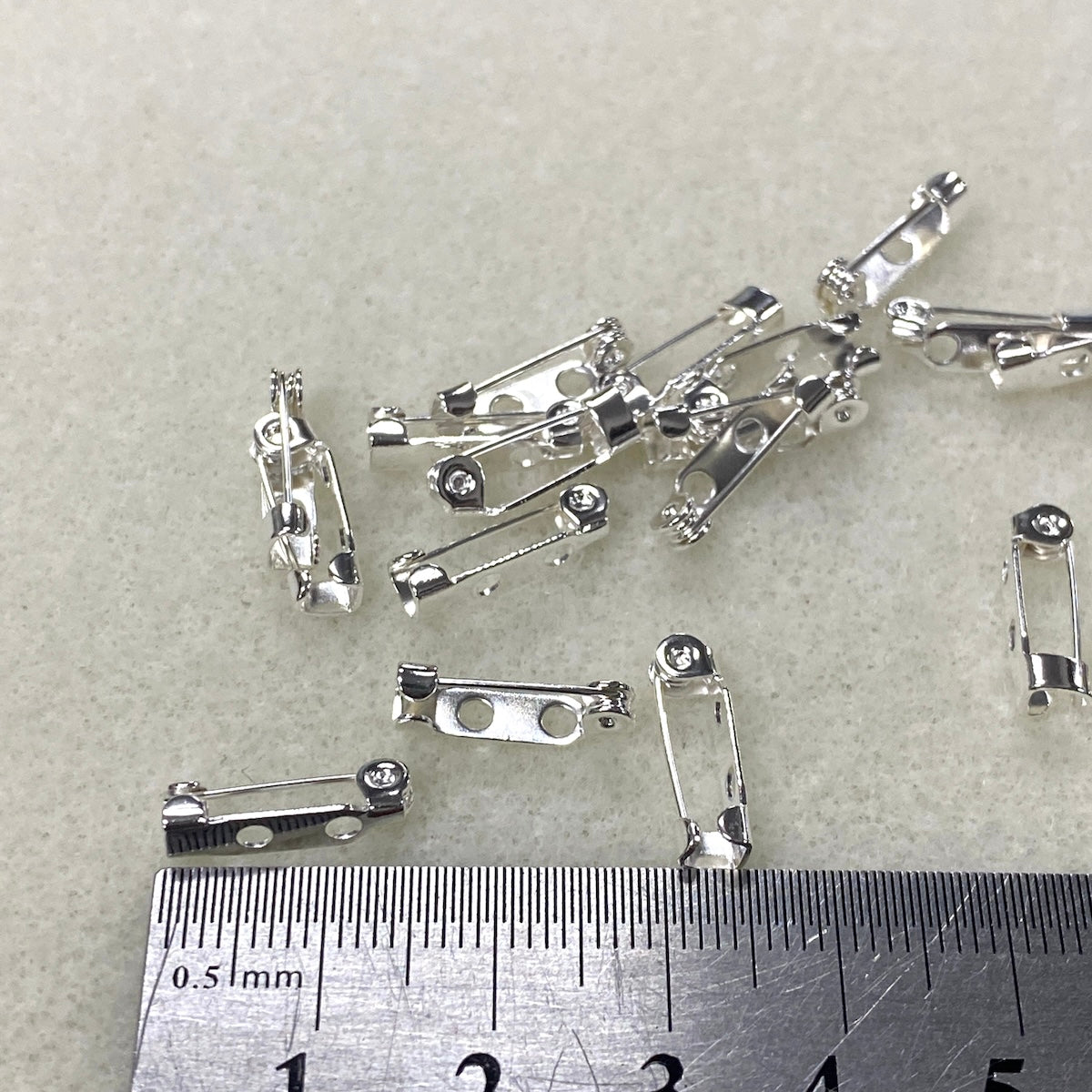 Small metal brooch pins on a gray background with a ruler for scale.
