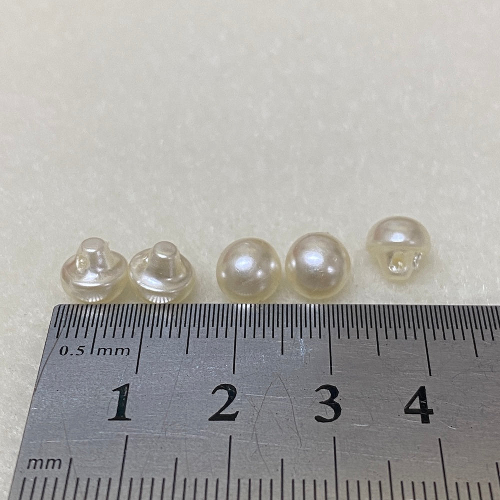 Five pearl buttons on a ruler for scale measurement.