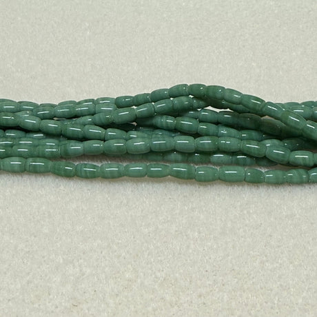 Green hand made tube Indonesian glass beads on a light gray background