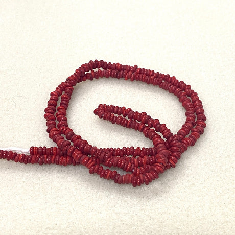 A strand of small, dark red, textured beads coiled on a light beige textured background.