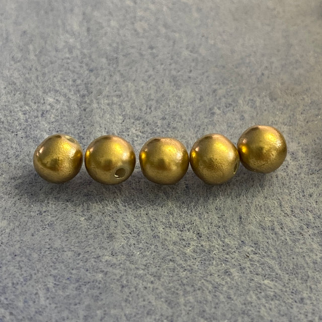 Five small metallic gold beads arranged in a row on a textured gray background.
