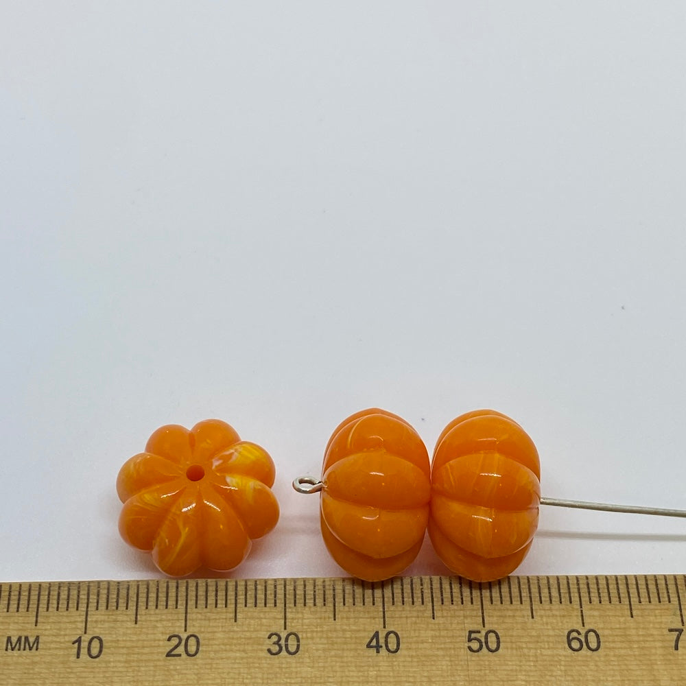 vibrant coloured pumpkin shaped beads against a ruler for size on a white background for the purposes of making craft and jewelry