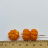 vibrant coloured pumpkin shaped beads against a ruler for size on a white background for the purposes of making craft and jewelry
