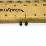 Two black beads next to a ruler for size reference on a white background