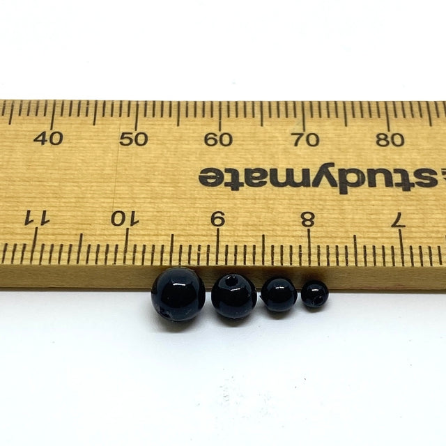 Four black beads lined up on a white surface with a ruler for scale.