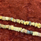 A close up of colored desert sand color faience beads arranged in lines, with varying shapes and textures.