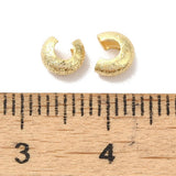 close up of 2 crimp covers with textured gold surface next to a wood ruler with sizes