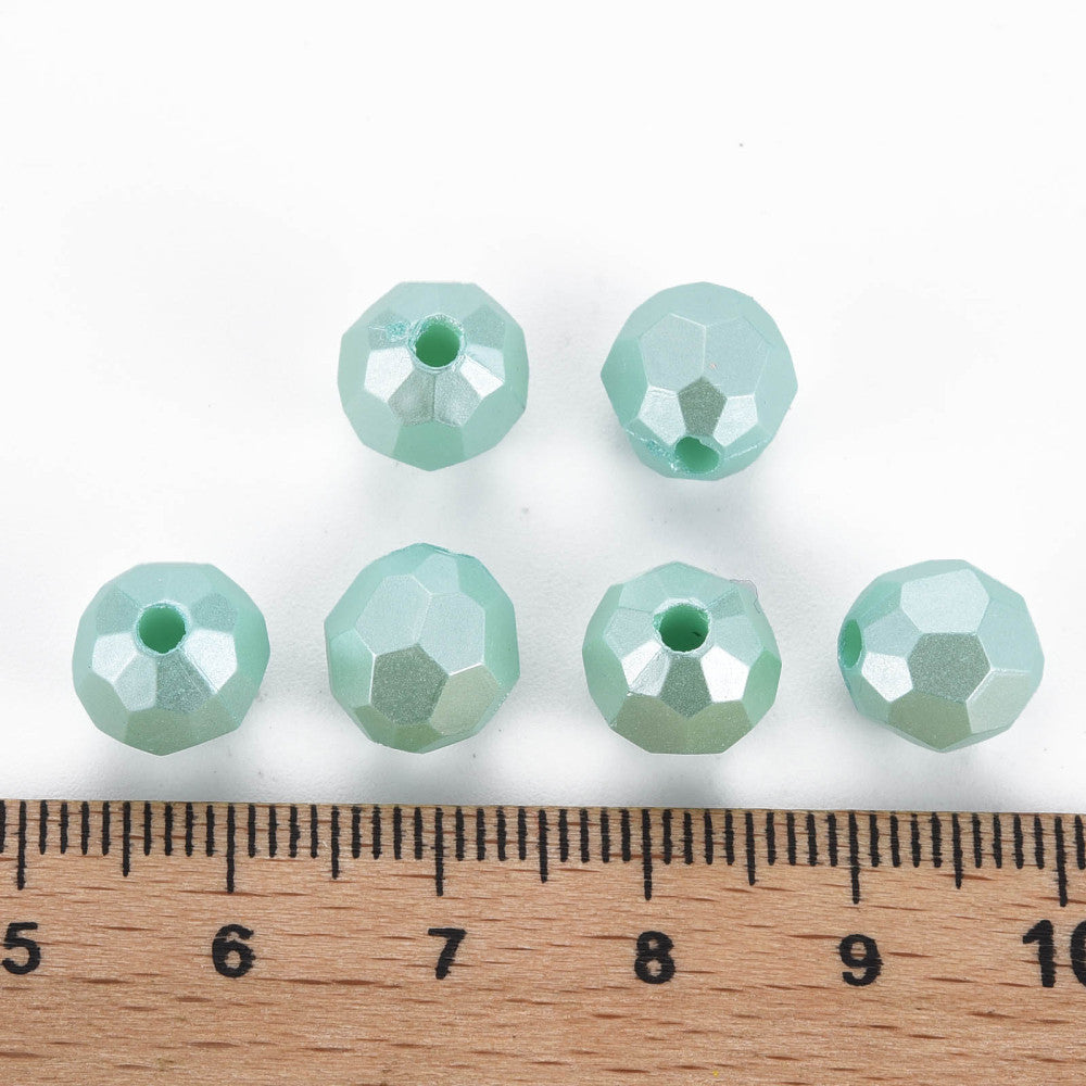 six faceted mint green glass beads arranged above a wooden ruler on a white background, showing their size.