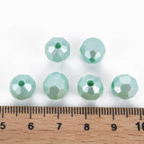 six faceted mint green glass beads arranged above a wooden ruler on a white background, showing their size.