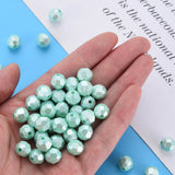 A hand holding a pile of faceted round beads in a pale mint green color, with a few additional beads scattered on a blue and white background.