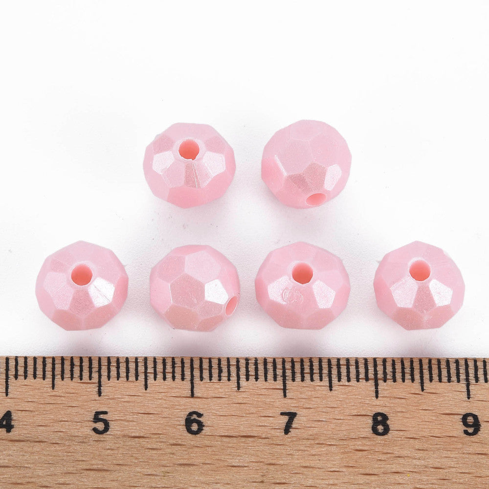 six faceted light pink beads arranged above a wooden ruler on a white background, showing their size.