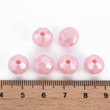 six faceted light pink beads arranged above a wooden ruler on a white background, showing their size.