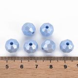 six faceted light blue beads arranged above a wooden ruler on a white background, showing their size relative to the measurement scale.