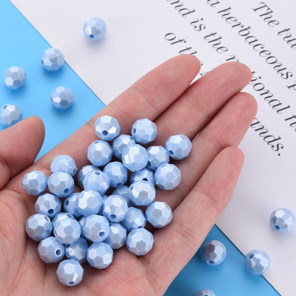 A hand holding a pile of light blue faceted round beads, with additional loose beads scattered on a blue and white background with printed text.