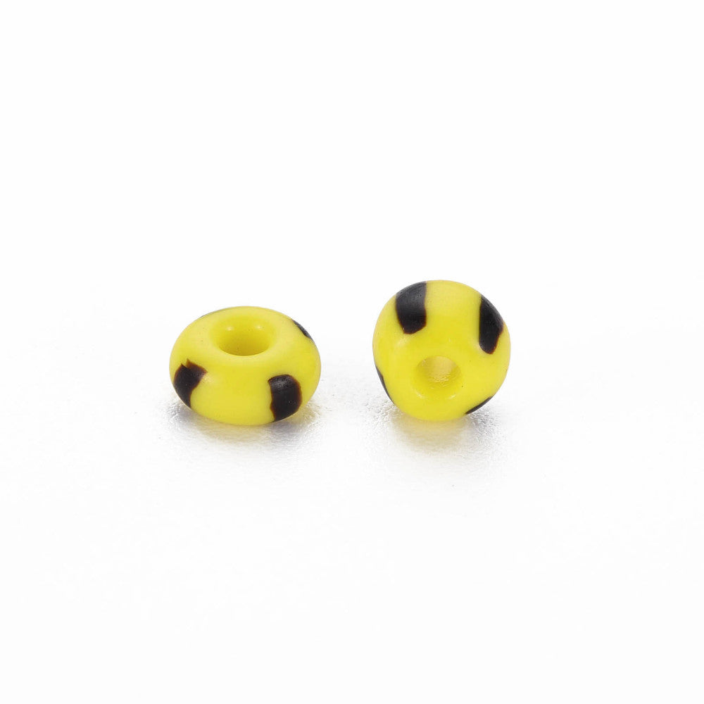 Two yellow glass seed beads with black stripes on a white background