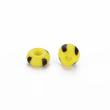 Two yellow glass seed beads with black stripes on a white background