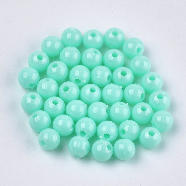 A pile of round opaque pale turquoise acrylic beads with visible holes for threading.