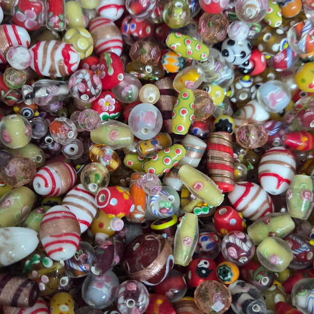 A dense pile of colorful glass lampwork beads with various patterns including stripes, polka dots, swirls, and floral motifs in red, yellow, green, white, and brown.