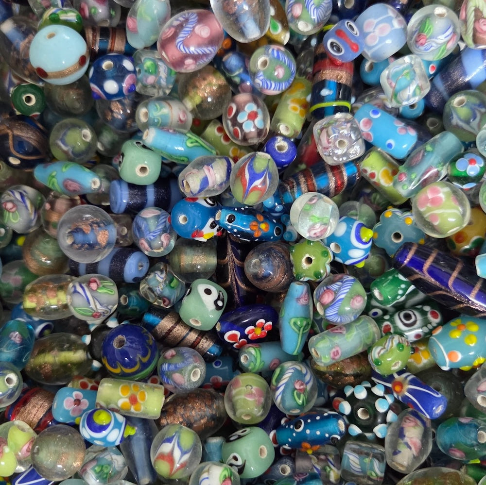 A dense pile of colorful glass lampwork beads with various patterns, including floral, geometric, and swirl designs in blue, green, purple, yellow, and white.