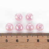 Six shiny pink pearl beads lined up on a wooden ruler for size reference.