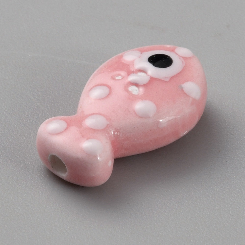 Pink fish-shaped bead with white spots and a black eye on a gray background