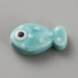 Turquoise fish-shaped bead with white spots and a black eye on a gray background