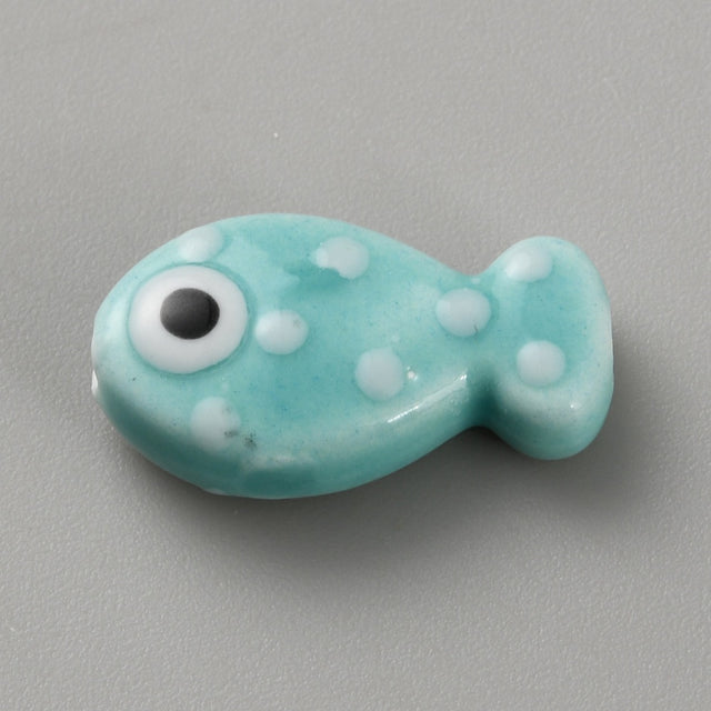 Turquoise fish-shaped bead with white spots and a black eye on a gray background