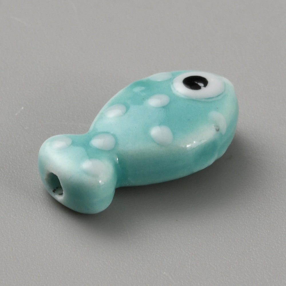 Turquoise fish-shaped bead with white spots and a black eye on a gray background