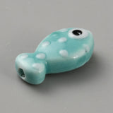 Turquoise fish-shaped bead with white spots and a black eye on a gray background