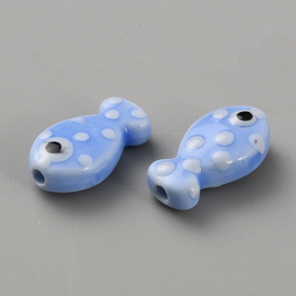 Two blue glass fish beads with white polka dots on a gray background