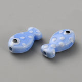 Two blue glass fish beads with white polka dots on a gray background