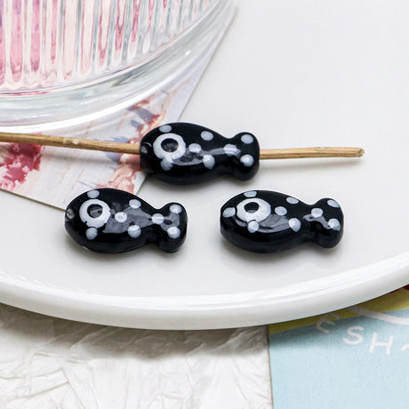 Black and white fish-shaped beads on a stick with a white plate and colorful background