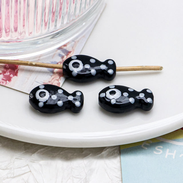 Black and white fish-shaped beads on a stick with a white plate and colorful background