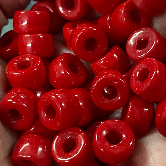 A close-up of glossy red pony beads with central holes, piled together in a hand.