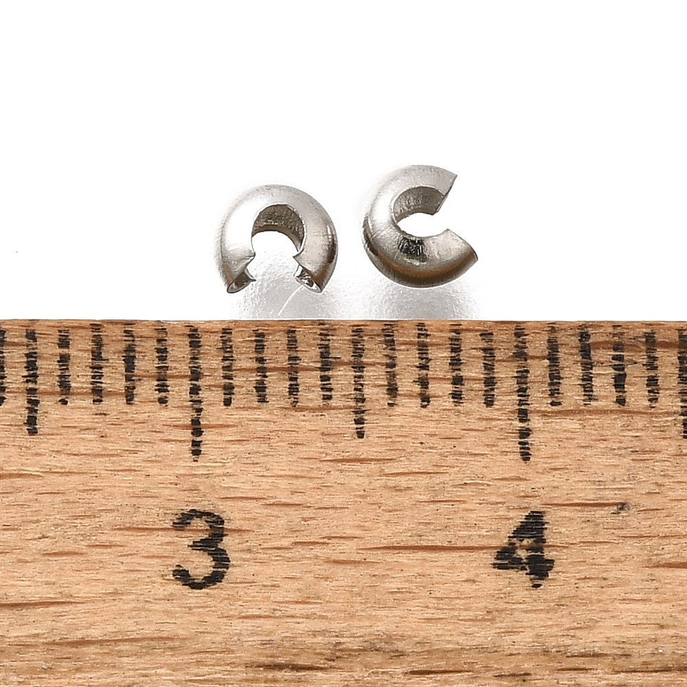 a collection of anti tarnish finished crimp cover beads on a white background with a wood ruler to demonstrate scale