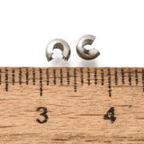 a collection of anti tarnish finished crimp cover beads on a white background with a wood ruler to demonstrate scale