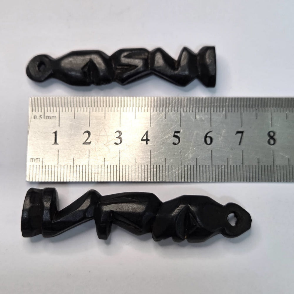 Two black wooden african folk art carvings on a white background with a ruler to show scale
