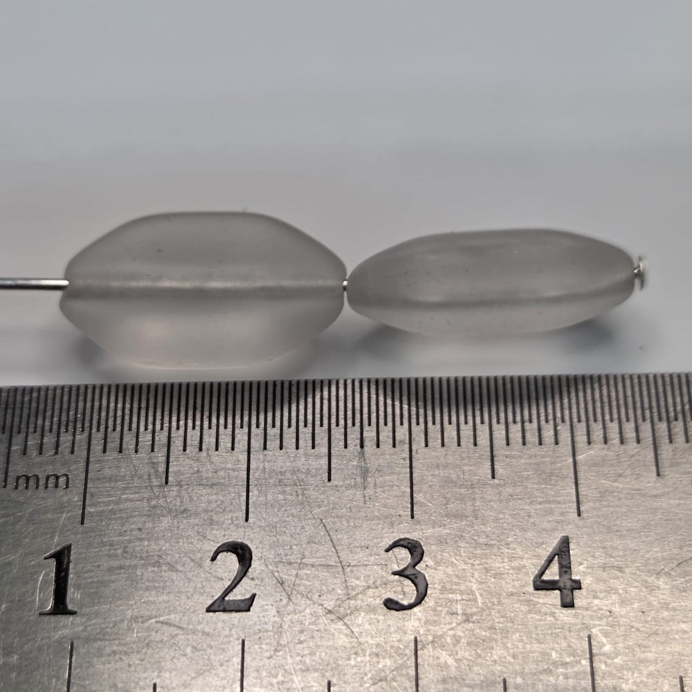 Close-up of white shield-shaped beads with a white background next to a ruler to show size