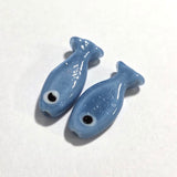 two sardine glass fish shape beads on a white surface