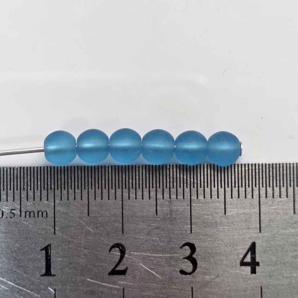 Blue beads on a needle with a ruler for scale on a white background