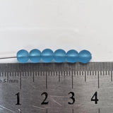 Blue beads on a needle with a ruler for scale on a white background