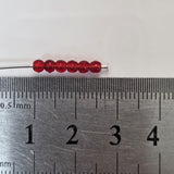 Red beads on a metal rod with a ruler for scale on a white background