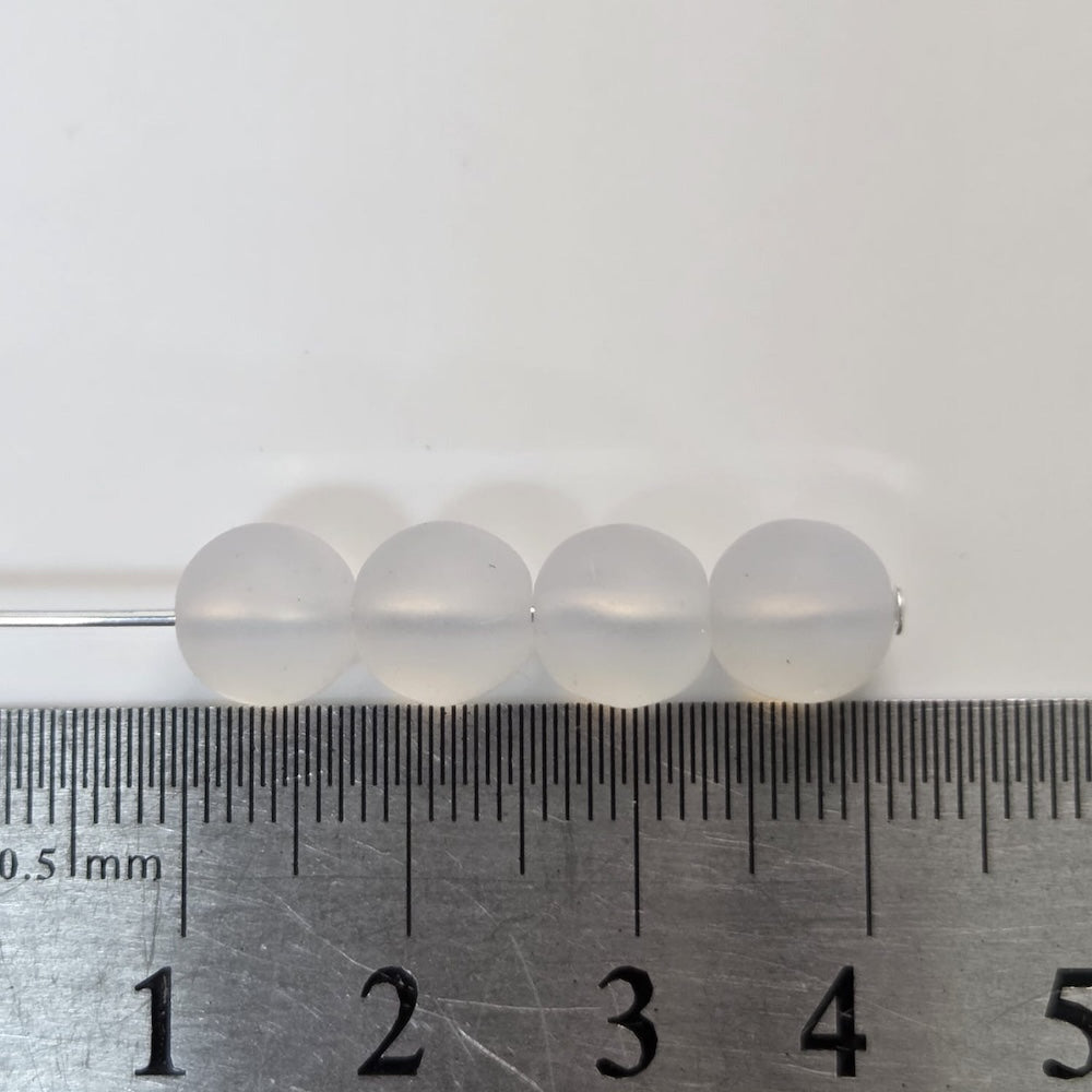 four round glass beads next to a ruler on a white background