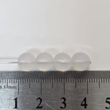 four round glass beads next to a ruler on a white background