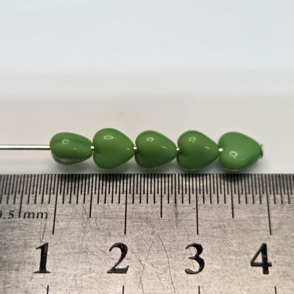 Green heart-shaped beads on a metal rod with a ruler below for scale.