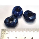 Three blue stone look beads with a ruler for scale on a white background