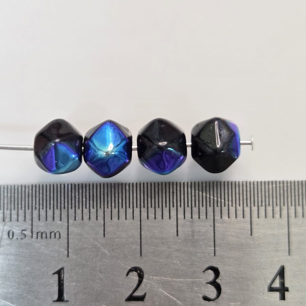 Four blue and black beads on a metal rod with a ruler for scale.