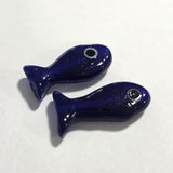 two glass dark blue fish beads on a white surface