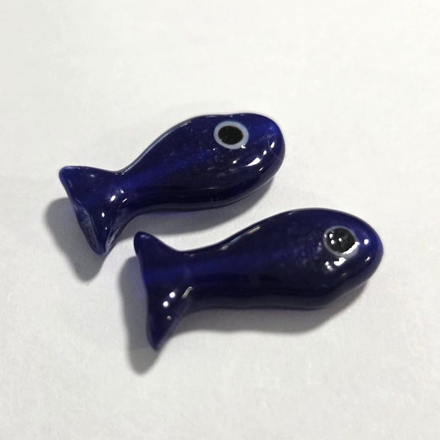 two glass dark blue fish beads on a white surface